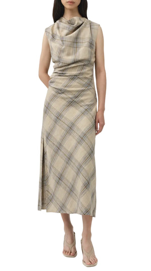 A person models the Simkhai Burke Draped Midi Dress, featuring a beige plaid pattern, cowl neckline, sleeveless cut, and side slit, styled with heeled sandals for a chic look against a white background.