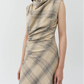 A woman wears the Simkhai Burke Draped Midi Dress in beige plaid, featuring a sleeveless design, cowl neckline, and ruched details, standing against a plain light background.