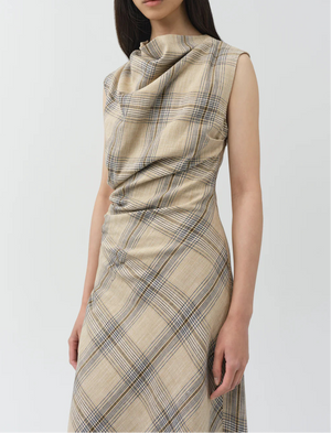 A woman wears the Simkhai Burke Draped Midi Dress in beige plaid, featuring a sleeveless design, cowl neckline, and ruched details, standing against a plain light background.