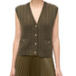 A woman wears the Simkhai Perrie Vest—an olive green, sleeveless, cable-knit cashmere vest with gold buttons—paired with a pleated skirt.