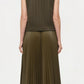 A person with short, straight hair is shown from the back wearing the Simkhai Perrie Vest, a sleeveless dark green cable knit top with a V-neckline, paired with a pleated skirt and black knee-high boots.