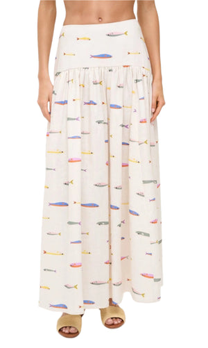 A person wearing the Staud Procida Linen Skirt—a long, white maxi skirt with a colorful sardines print—paired with beige open-toe sandals.