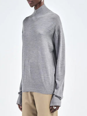 A person wearing the Maria McManus Fine Gauge Mock Neck Sweater in heather grey with beige pants, standing against a plain background.