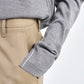 A person wearing the Maria McManus Fine Gauge Mock Neck Sweater in heather grey with white piping, paired with beige trousers and their hand in a pocket.