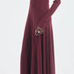 A person in the Maria McManus Rib Godet Dress—long-sleeved, floor-length merlot—with black pointed shoes stands against a plain light background.