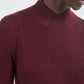 A person wearing the Maria McManus Rib Godet Dress in burgundy merlot with long sleeves, a mock neckline, and geometric silver earrings.