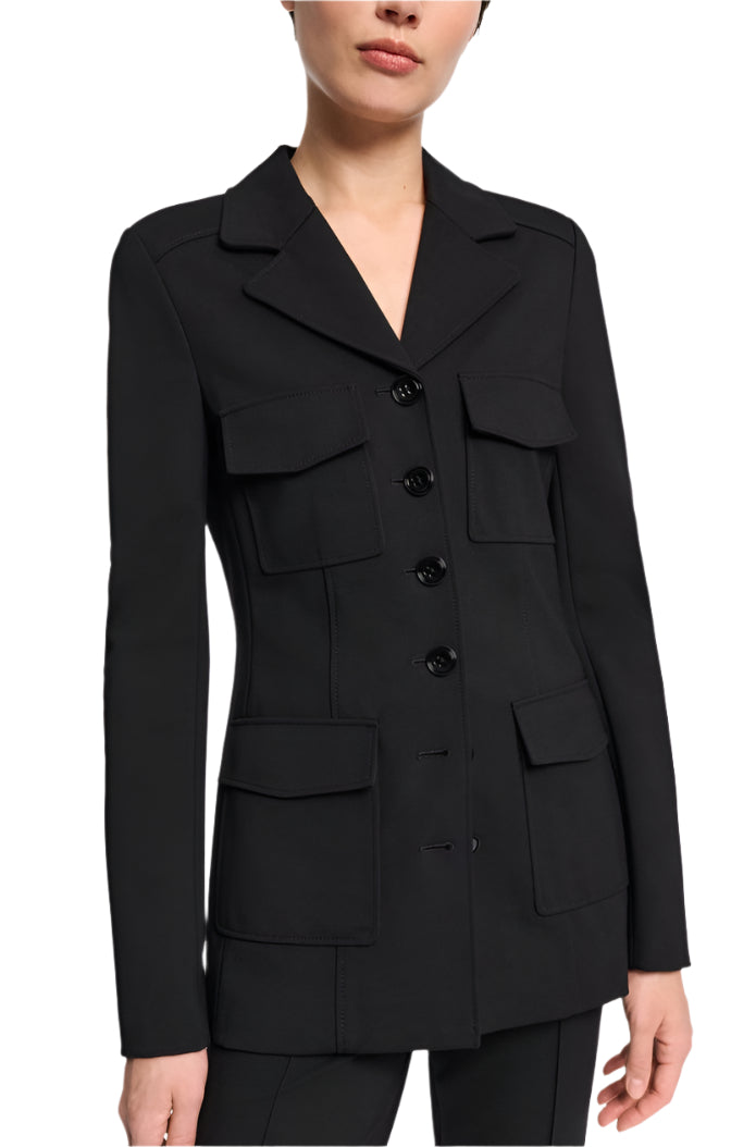 A person is wearing the Dorothee Schumacher Emotional Essence Jacket, a black tailored blazer with notched lapels and four pockets, featuring button closure. This stylish piece combines Punto Milano fabric for a sophisticated shirt-jacket hybrid look.