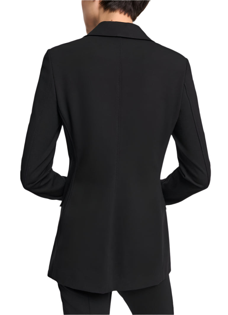 A person stands with hands on hips wearing the Dorothee Schumacher Emotional Essence Jacket, a black tailored blazer with long sleeves and a notched lapel.