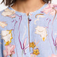 Close-up of someone in a Dorothee Schumacher Floral Power Mini Dress. The blue linen shift dress features a round neckline with pink, yellow, and white floral patterns. Voluminous sleeves add elegance, while the person's head is partially visible.