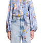 A person wearing the Dorothee Schumacher Floral Power Blouse, a light blue printed linen blouse with long sleeves and a V-neckline, paired with high-waisted light blue jeans.