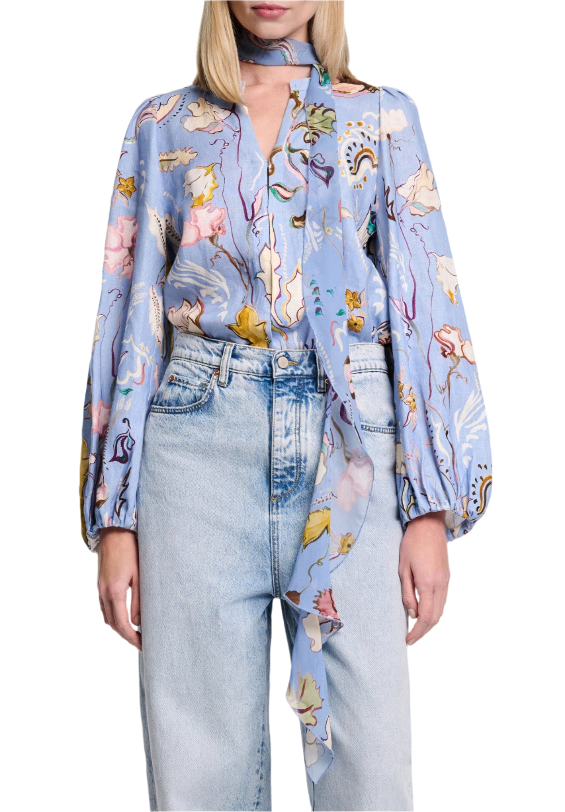 A person wearing the Dorothee Schumacher Floral Power Blouse, a light blue printed linen blouse with long sleeves and a V-neckline, paired with high-waisted light blue jeans.