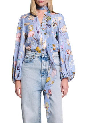 A person wearing the Dorothee Schumacher Floral Power Blouse, a light blue printed linen blouse with long sleeves and a V-neckline, paired with high-waisted light blue jeans.