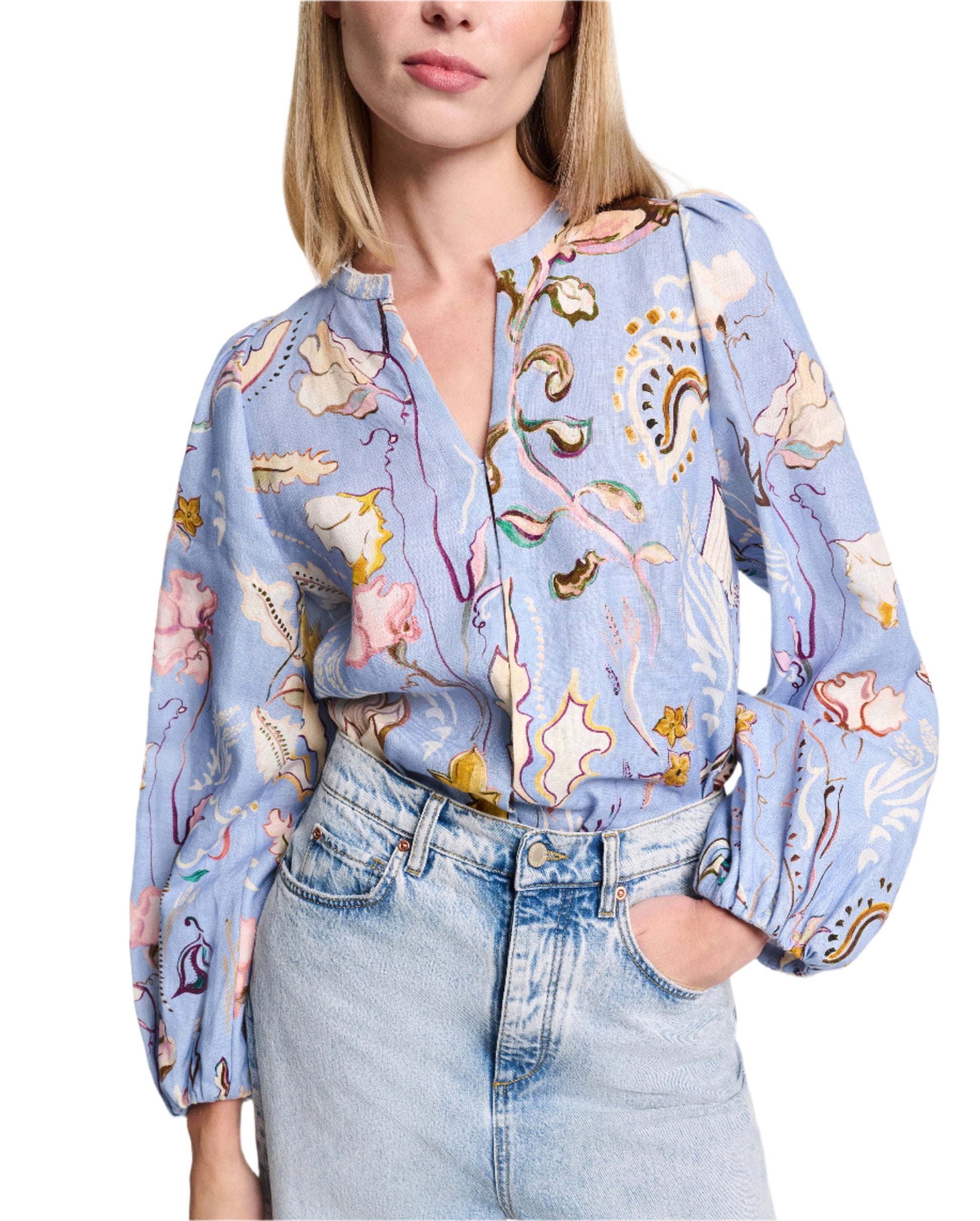 A person is styled in the Dorothee Schumacher Floral Power Blouse, featuring a V-neckline and long sleeves. They pair it with light blue jeans and a silk georgette scarf, effortlessly draping around their neck for an elegant touch, while posing with one hand in the pocket.