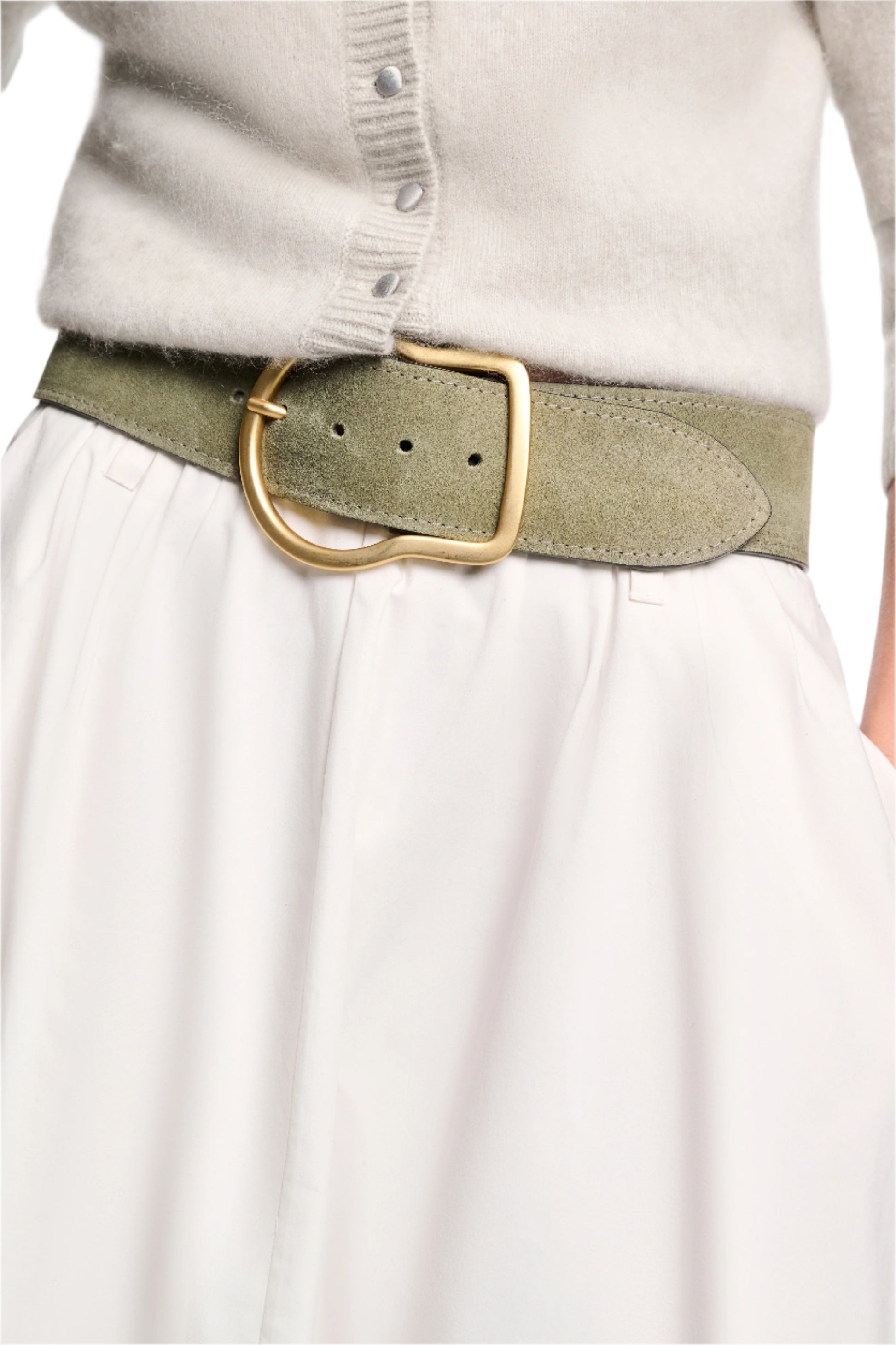 A person wears a light gray sweater with a white skirt, accented by Dorothee Schumacher's Suede Sensation Belt in olive green suede with a large gold buckle and chic curved design.