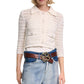 A woman wears the Dorothee Schumacher Precise Pointelle Jacket—a white crocheted button-up cardigan with graphic pointelle details—paired with a white top, blue jeans, and a brown belt featuring a large decorative buckle.