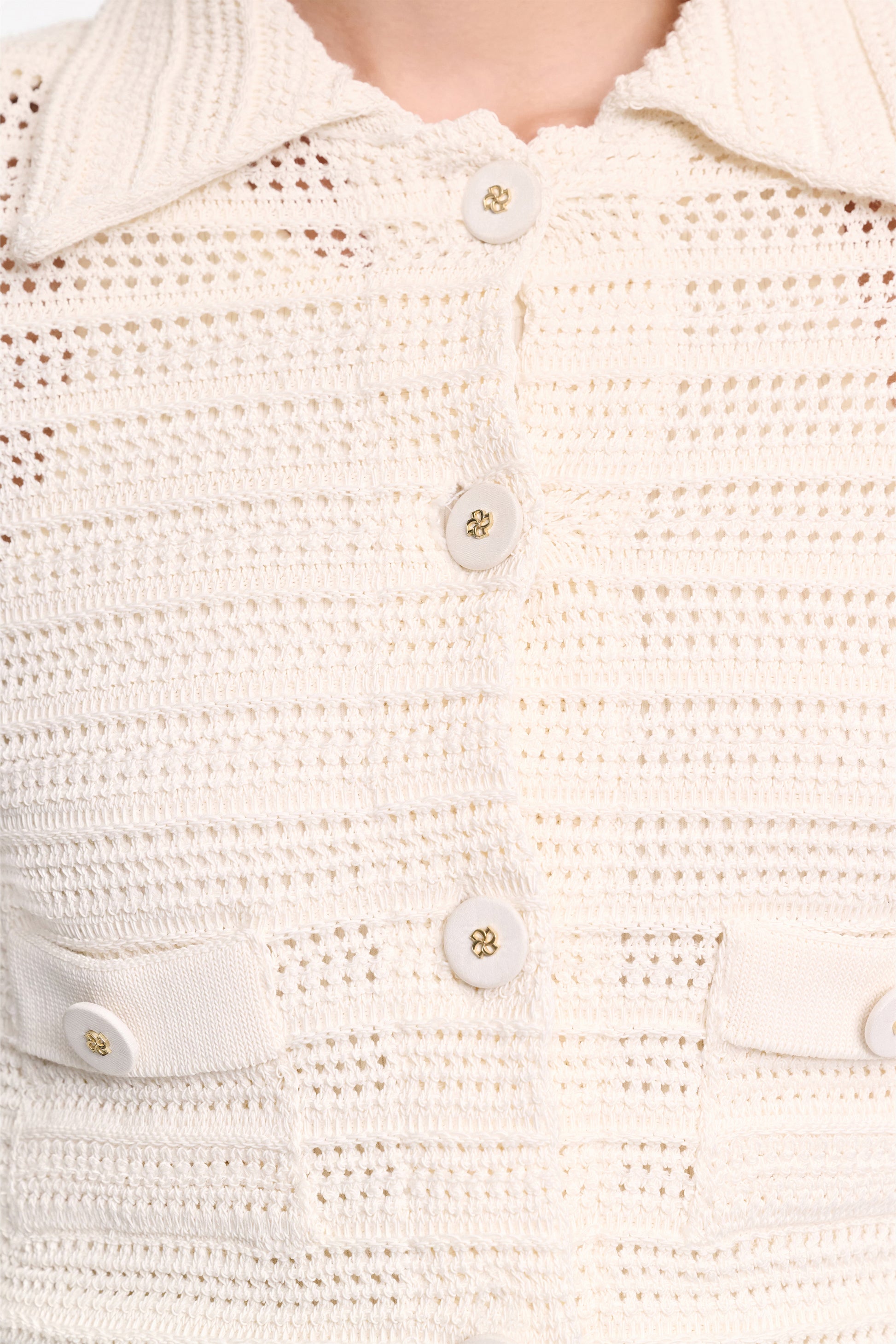 Close-up of the Dorothee Schumacher Precise Pointelle Jacket—a cream-colored, crocheted shirt with a graphic pointelle pattern, four buttons, and two chest pockets, worn by a person.