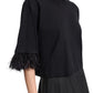 A woman wears the Dorothee Schumacher Feminine Favorites Shirt, a black boxy cotton T-shirt with ostrich feather trim on the sleeves, paired with a black skirt and shown from shoulders to waist.