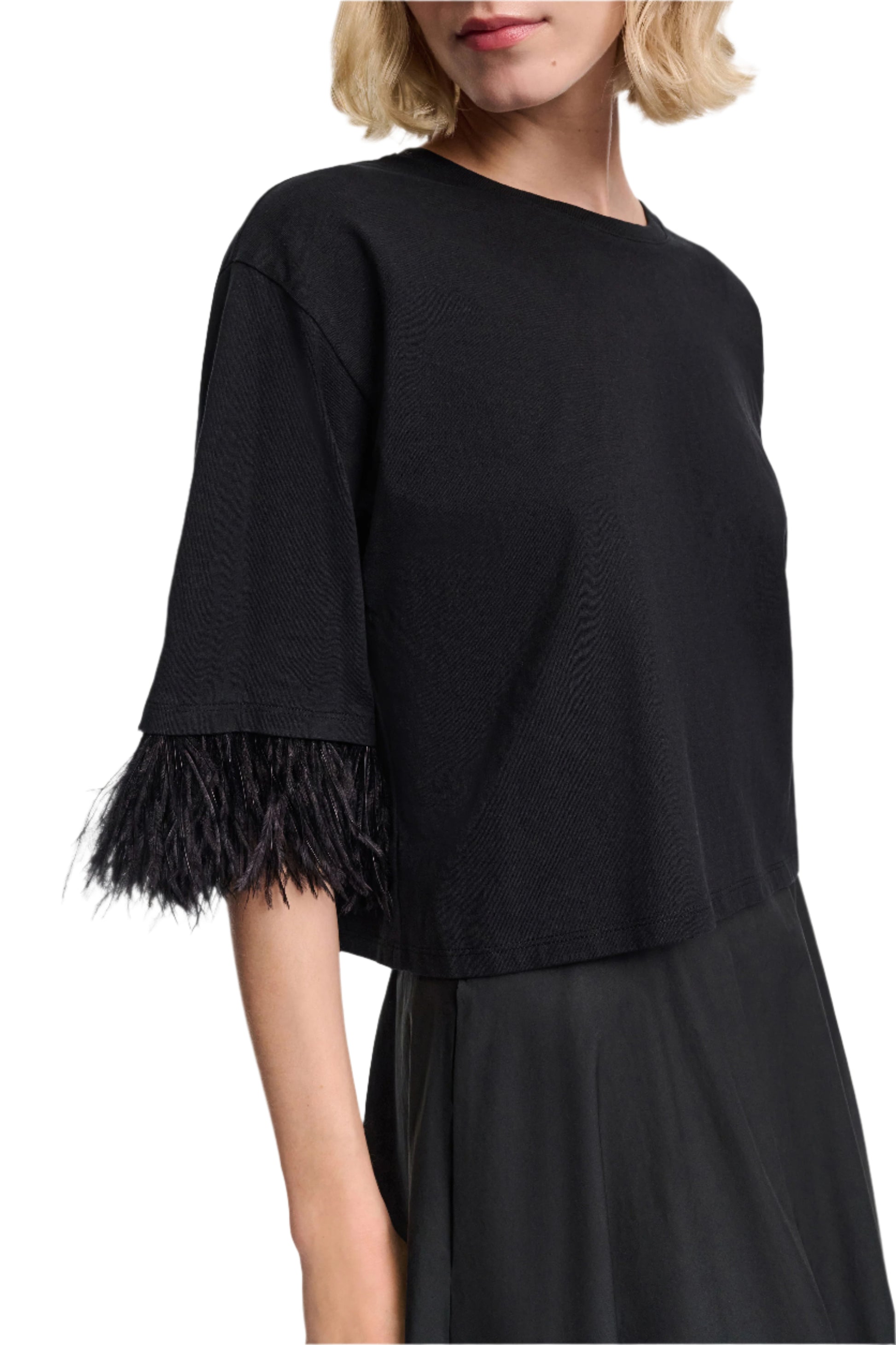 A woman wears the Dorothee Schumacher Feminine Favorites Shirt, a black boxy cotton T-shirt with ostrich feather trim on the sleeves, paired with a black skirt and shown from shoulders to waist.