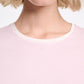 A close-up shows a person with short blonde hair wearing the Dorothee Schumacher All Time Favorites Shirt, a fitted light pink top with a white collar, highlighting its comfortable stretch cotton fabric. Only the lower face and upper torso are visible.