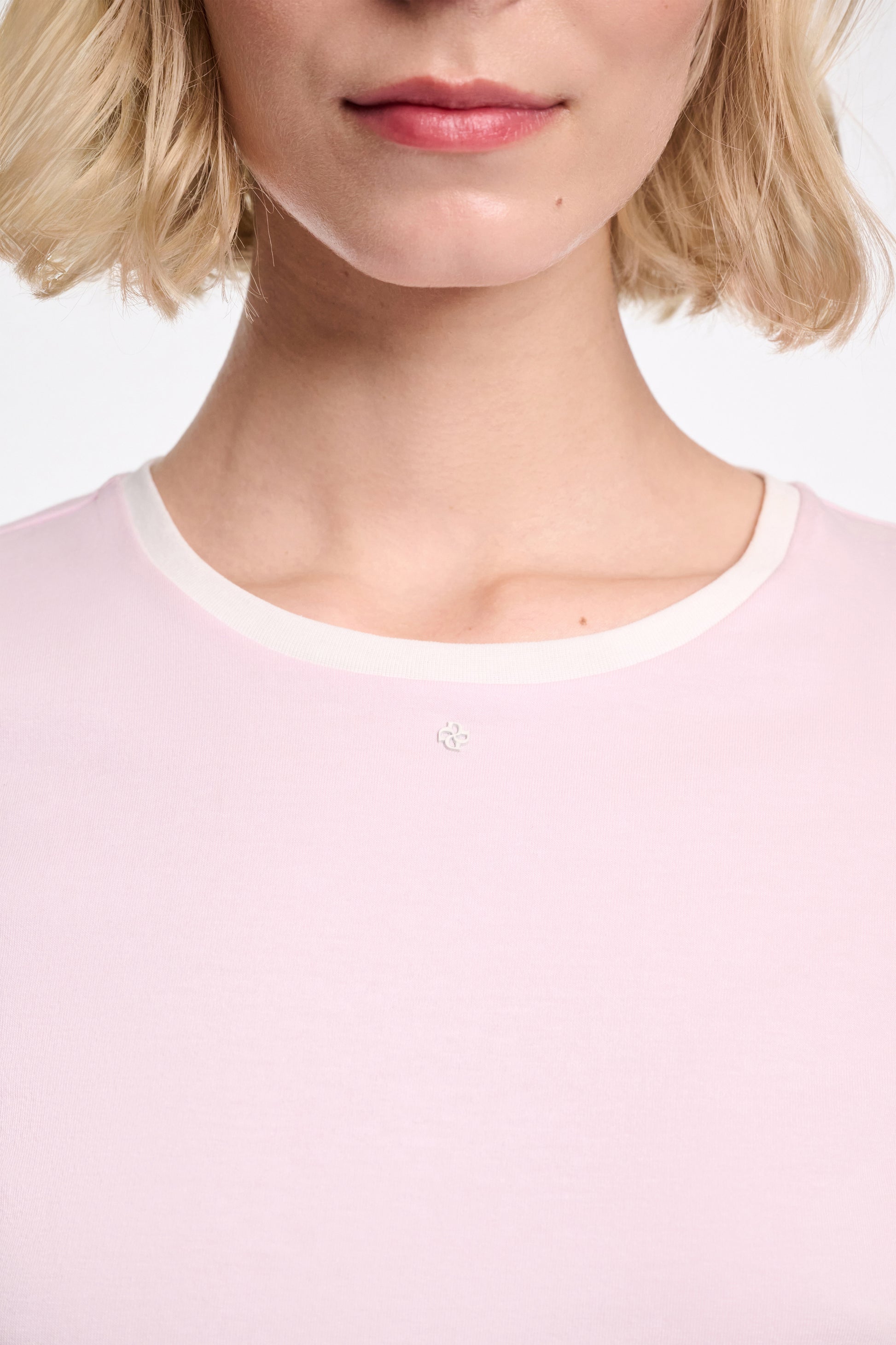 A close-up shows a person with short blonde hair wearing the Dorothee Schumacher All Time Favorites Shirt, a fitted light pink top with a white collar, highlighting its comfortable stretch cotton fabric. Only the lower face and upper torso are visible.