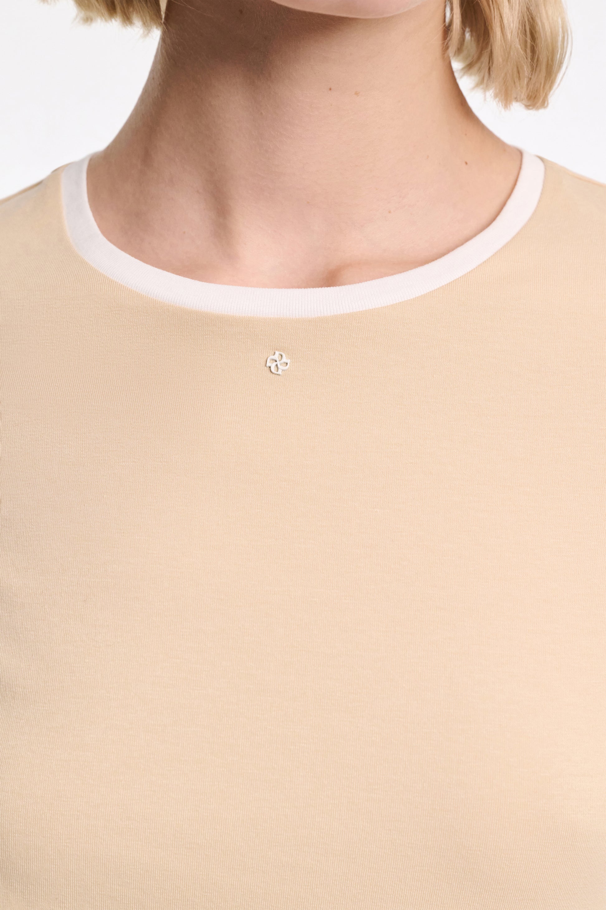 A close-up of a person wearing the All Time Favorites Shirt by Dorothee Schumacher, featuring a white collar, small metallic emblem near the neckline, and crafted from comfortable stretch cotton for an effortless fitted style.