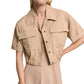 A woman wears the Dorothee Schumacher Poplin Power Cropped Blouse, a tan short-sleeve blouse with front pockets and open collar, over a matching tan dress.