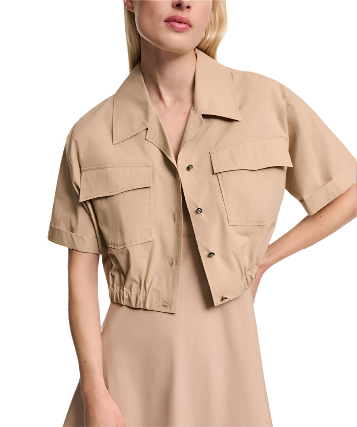 A woman wears the Dorothee Schumacher Poplin Power Cropped Blouse, a tan short-sleeve blouse with front pockets and open collar, over a matching tan dress.