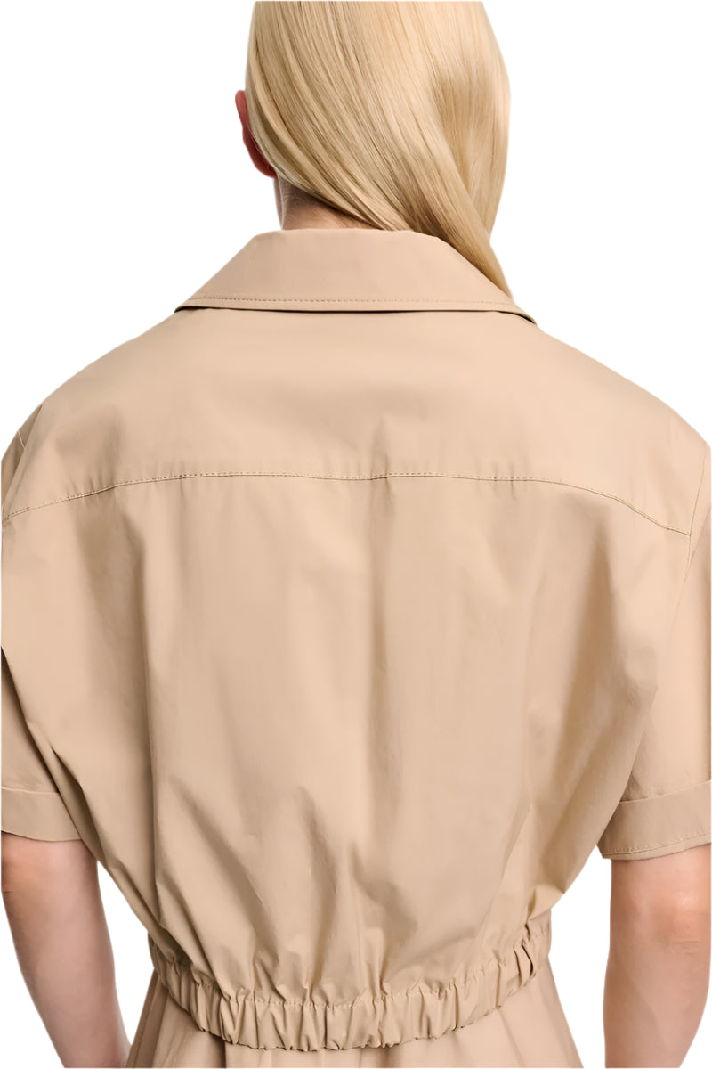 A person with long blonde hair is shown from the back wearing Dorothee Schumacher’s Poplin Power Cropped Blouse—a beige, short-sleeved cotton poplin top featuring an open collar and elastic cinched waist.