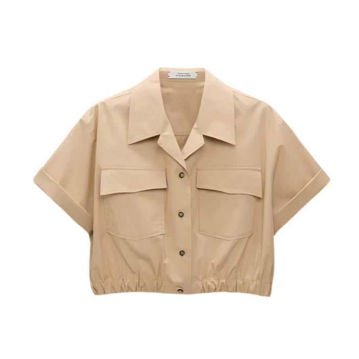 The Poplin Power Cropped Blouse by Dorothee Schumacher is a beige cotton poplin top featuring short sleeves, an open collar, two large chest pockets, and an elastic hem for a cropped fit.