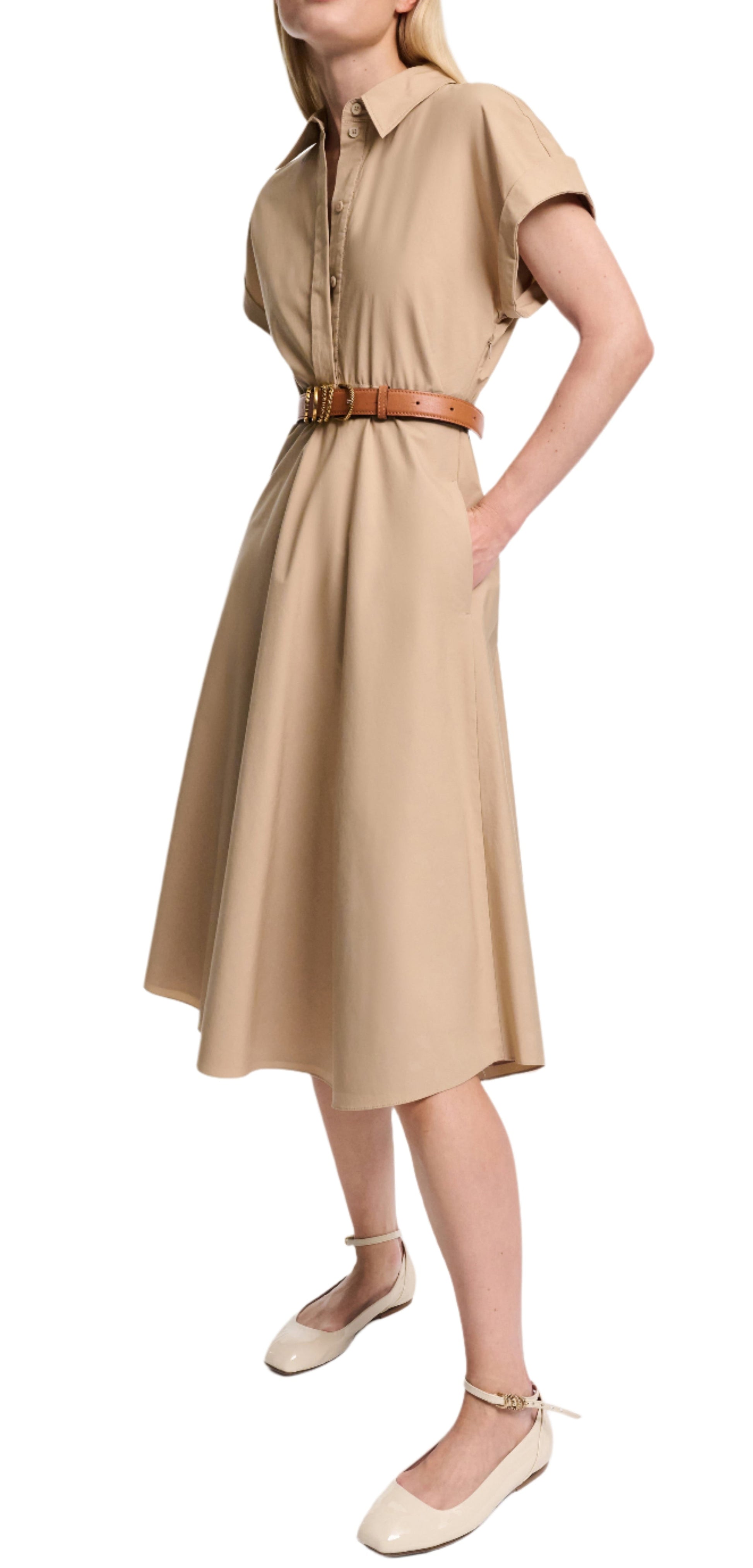 A woman poses with one hand on her hip, wearing the Dorothee Schumacher Poplin Power Dress—a beige cotton shirtdress with a tailored waist, tan belt, and cream ankle-strap flats.