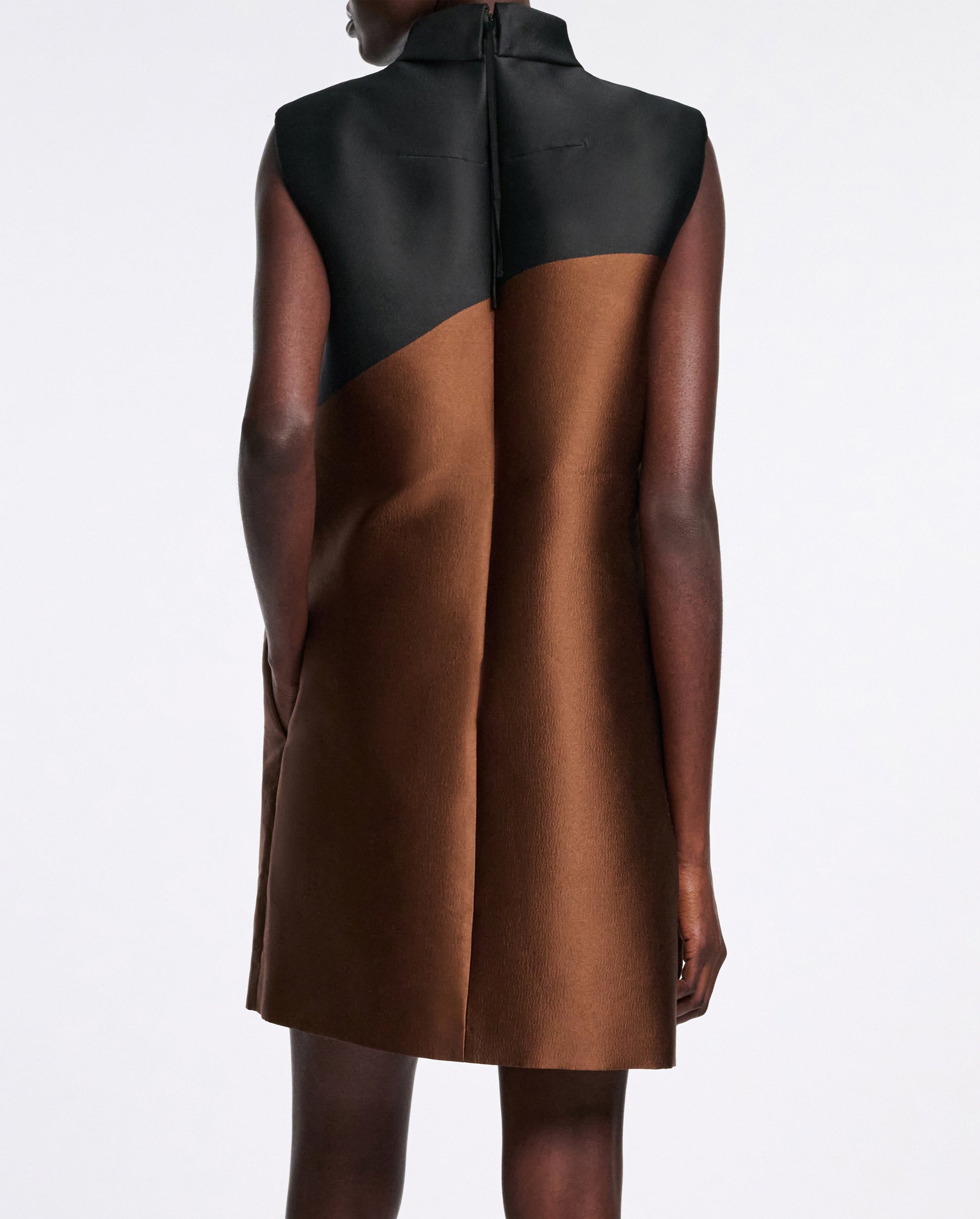 A person in the Dorothee Schumacher Soft Petal Dress, featuring a sleeveless black top and brown skirt inspired by Italian artistry, is photographed from the back against a plain background.