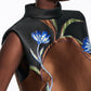 A person wearing the Soft Petal Dress by Dorothee Schumacher, a sleeveless brown and black stand collar cloque jacquard dress with blue and white floral embroidery on the chest that highlights Italian artistry.