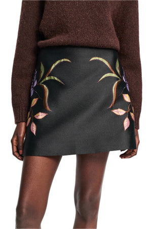A person wears the Dorothee Schumacher Soft Petal Mini Skirt, an A-line mini with a vibrant leaf and floral print near the hem, paired with a dark brown sweater—showcasing Italian-inspired artistry.