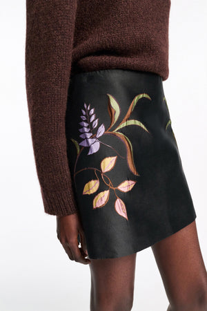 A person wears the Dorothee Schumacher Soft Petal Mini Skirt, an A-line piece with a floral print of purple flowers and yellow leaves, styled with a dark brown knit sweater to showcase refined Italian artistry.