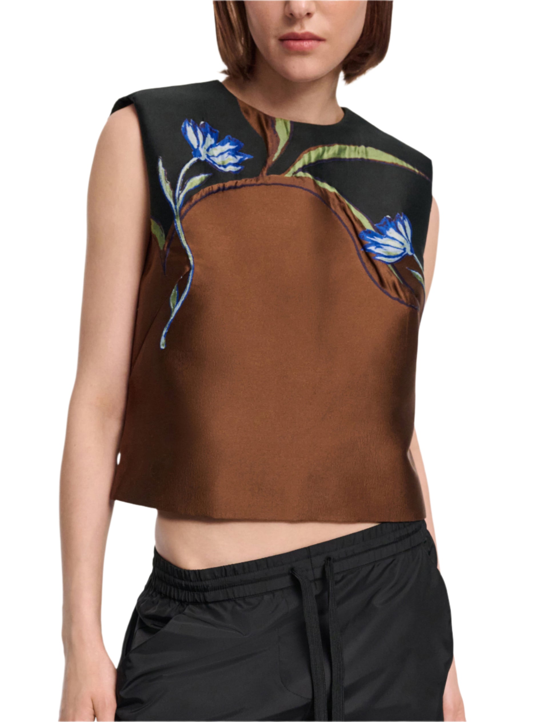 Woman wears the Soft Petal Top by Dorothee Schumacher—a sleeveless brown and black crop with blue floral print—paired effortlessly with black drawstring pants, evoking Italian-inspired artistry.