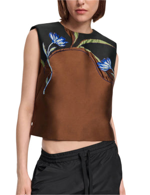 Woman wears the Soft Petal Top by Dorothee Schumacher—a sleeveless brown and black crop with blue floral print—paired effortlessly with black drawstring pants, evoking Italian-inspired artistry.
