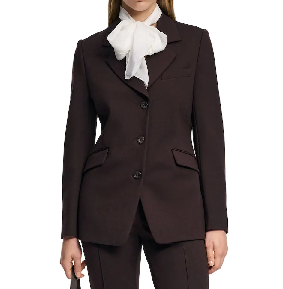 A person wears the Emotional Essence Jacket by Dorothee Schumacher, a dark espresso blazer with notch lapel, three buttons, and flap pockets, paired with a white sheer bow tie blouse against a plain background.