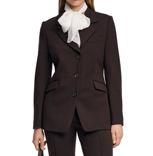 A person wears the Emotional Essence Jacket by Dorothee Schumacher, a dark espresso blazer with notch lapel, three buttons, and flap pockets, paired with a white sheer bow tie blouse against a plain background.