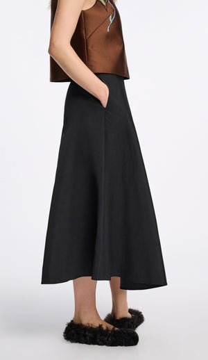 A person stands against a white background wearing a sleeveless brown top, black furry flat shoes, and the Dorothee Schumacher Sporty Elegance Skirt—an elegant long black A-line skirt with pockets.