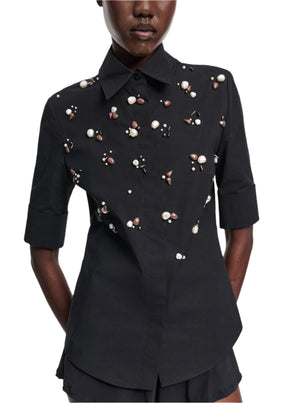 A person wears the Dorothee Schumacher Poplin Power Embellished Blouse, a fitted black cotton-poplin shirt with elbow-length sleeves, adorned with pearls and beads.