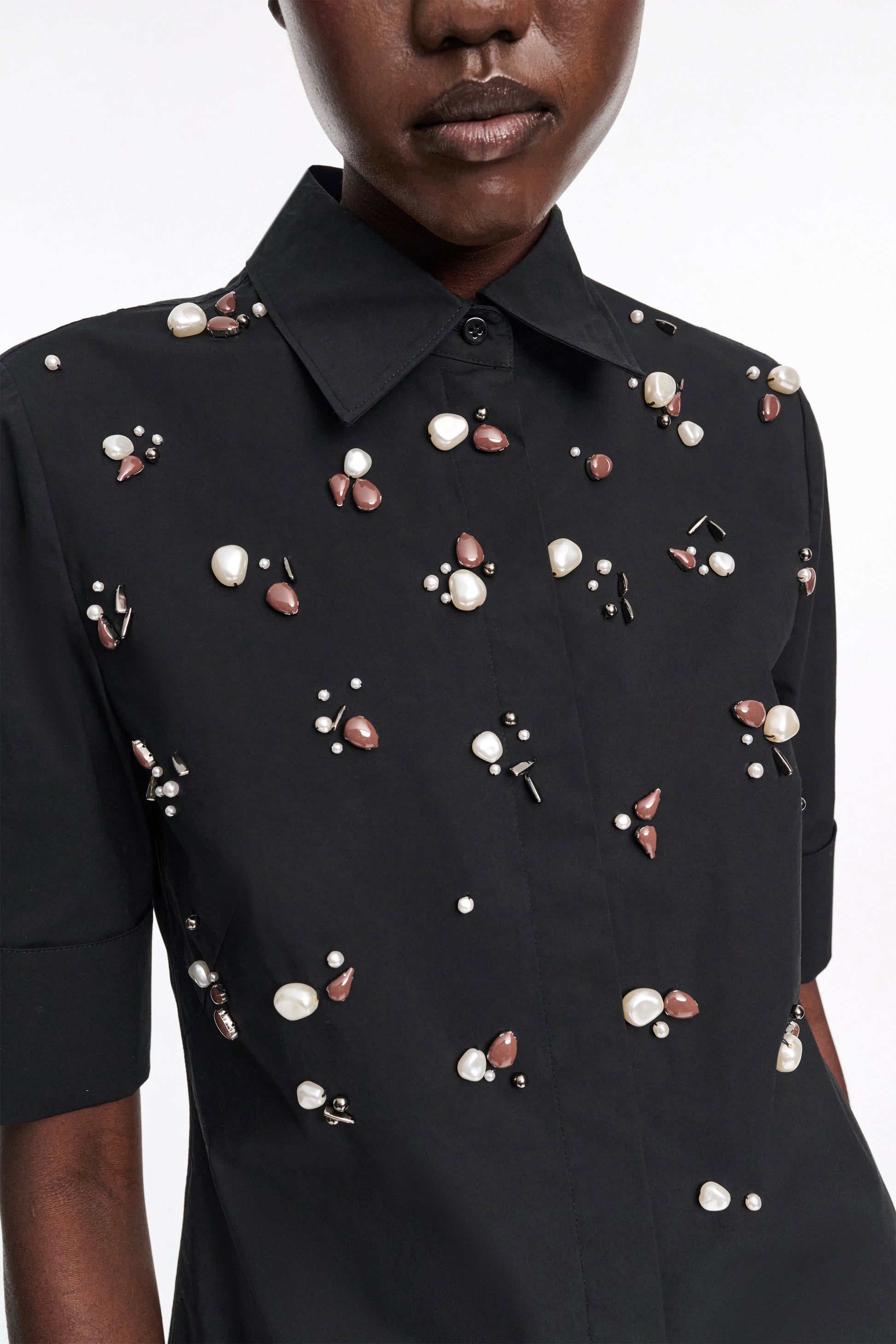 A person wears the Dorothee Schumacher Poplin Power Embellished Blouse, a black cotton-poplin shirt featuring clusters of pearl and brown bead details.