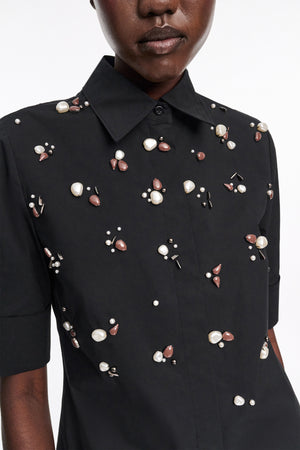 A person wears the Dorothee Schumacher Poplin Power Embellished Blouse, a black cotton-poplin shirt featuring clusters of pearl and brown bead details.