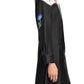 A woman wears the Seductive Bloom Maxi Dress by Dorothee Schumacher—a long-sleeved black silk shirtdress with a white yoke and blue floral embroidery—standing against a plain light background.