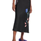 Someone wearing Dorothee Schumacher's Seductive Bloom Skirt—a black, bias-cut piece with floral motifs—paired with a light gray top and purple fuzzy slippers.