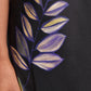 A close-up of a hand beside the Dorothee Schumacher Seductive Bloom Skirt, a black silk midi-skirt with a painted purple and yellow leaf design.