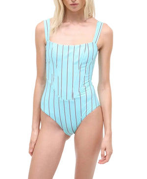 A woman wears the Staud Adelaide One Piece, a light blue swimsuit with vertical black stripes and supportive shoulder straps, shown from shoulders to upper thighs.