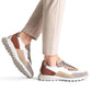 A person wearing beige pants and Magnanni Onyx Sneakers stands on tiptoe, displaying the luxury design of these multicolored suede sneakers with white soles, one foot raised.