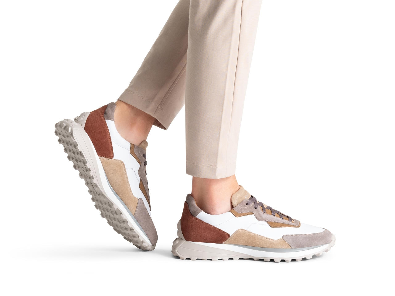 A person strides forward in beige pants and two-tone sneakers featuring a thick, textured sole. These Magnanni Onyx Sneakers exude luxury design, making every step feel as stylish as it is comfortable.