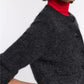Someone wears the Dorothee Schumacher Fluffy Statements Cardigan in dark gray over a red turtleneck sweater, with their arm bent and hand resting on their hip.