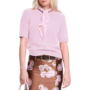 A woman wears the Dorothee Schumacher Fluffy Statements Pullover, a soft knit light pink short sleeve sweater, paired with a matching scarf and brown skirt with pink and white swirls, holding a white bag.